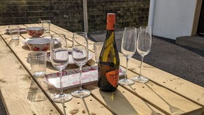 Un juego de mesa de picnic de madera al aire libre, con copas de vino, una botella de Prosecco y vajilla con estampado floral.