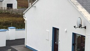 Edificio blanco con puerta y ventana azules, rodeado por una cerca.