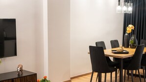 Un salon moderne doté d’un téléviseur à écran plat, d’une console en bois, d’un coin repas avec une table et des chaises, et d’un tapis à motifs.