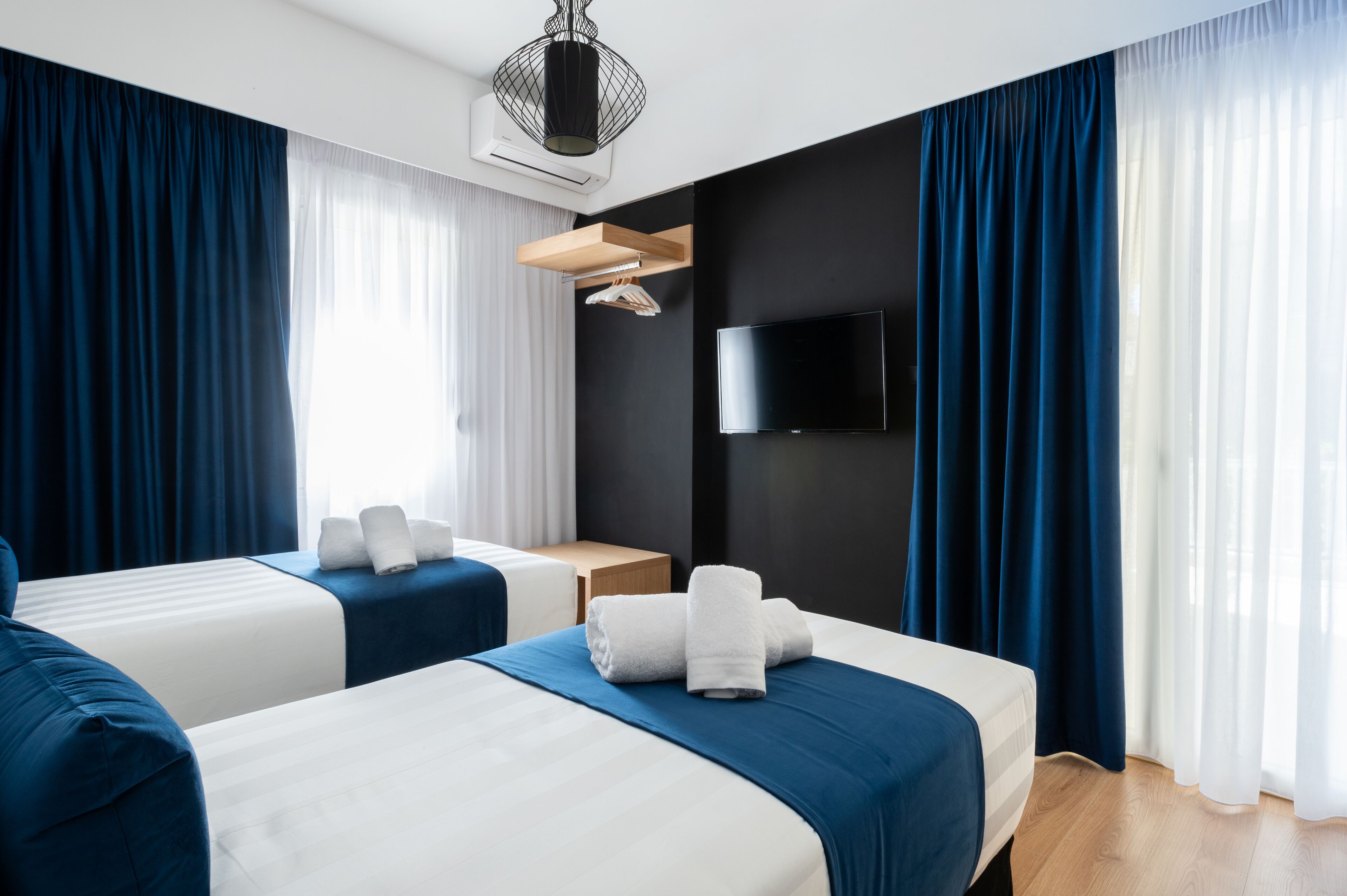A hotel room with two beds, a flat-screen TV, a wooden side table, and a ceiling light fixture.