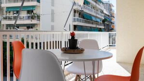 Un balcon avec une table ronde et quatre chaises, dont une est orange. Une plante en pot avec des fleurs rouges est posée sur la table.