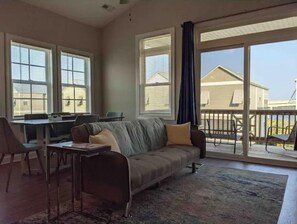Relax in this spacious living area with a comfortable sofa and dining table for two, leading to an outdoor patio.