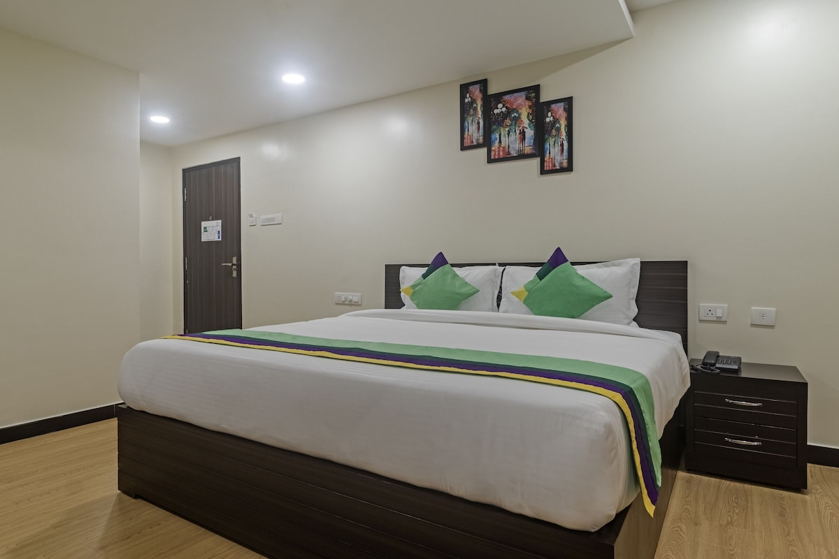 A hotel room with a large bed, a bedside table with a phone, and a door with a sign.