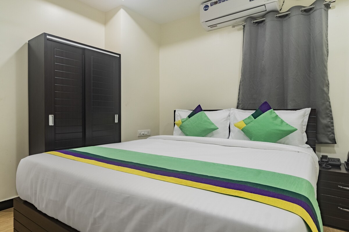 A hotel room with a bed, a wardrobe, a bedside table, and an air conditioning unit.