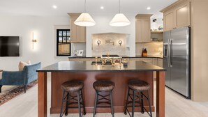 A modern kitchen with a large island, stainless steel appliances, pendant lighting, and a bar stool seating area.