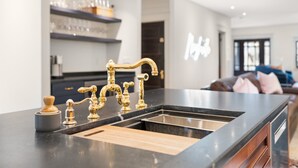A modern kitchen with a black countertop, gold faucets, and a wooden cutting board.