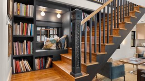 A modern staircase with wooden steps and black railings, surrounded by bookshelves filled with books and decorative pillows.