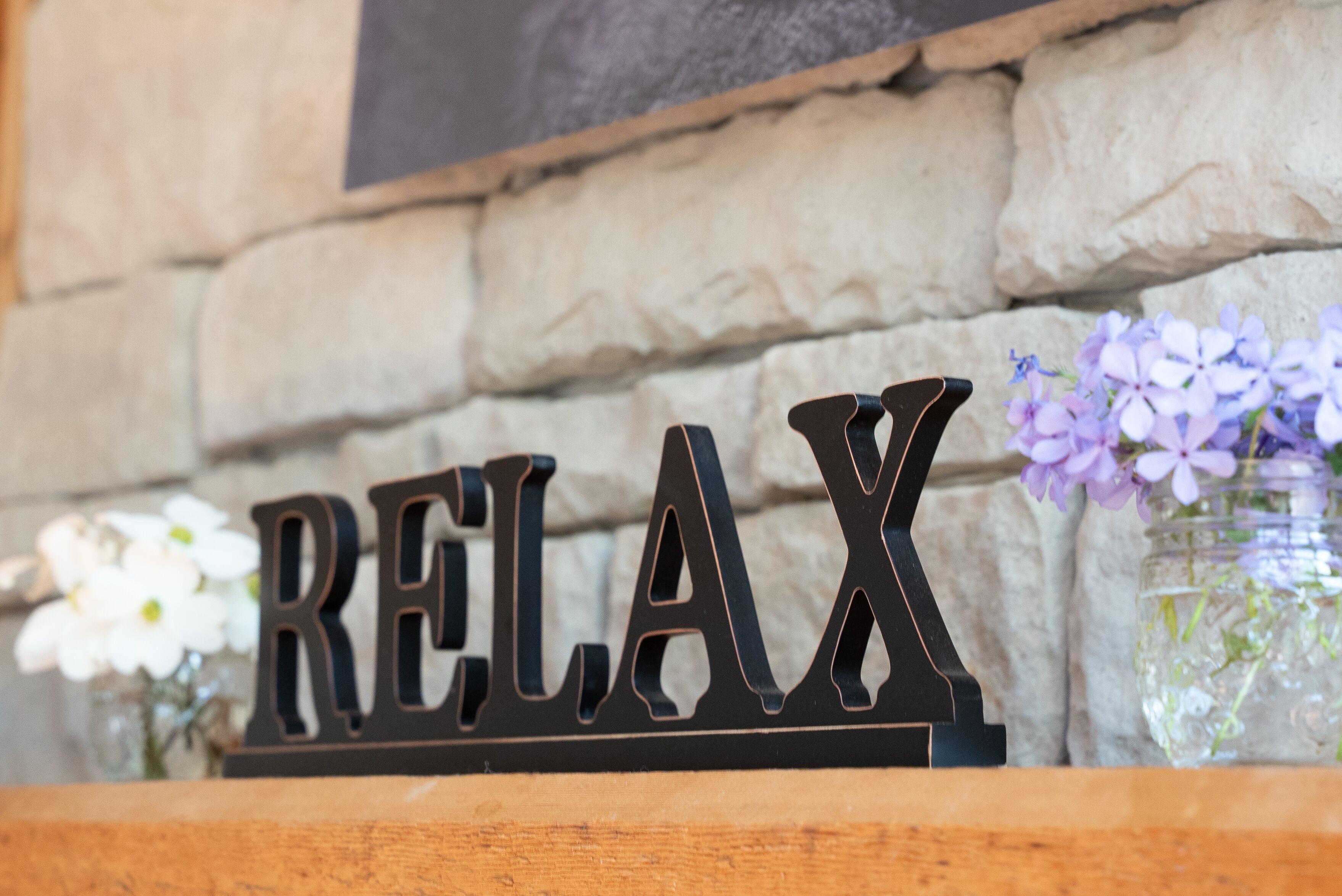 Une étagère en bois avec une pancarte indiquant « RELAX » et un vase de fleurs.