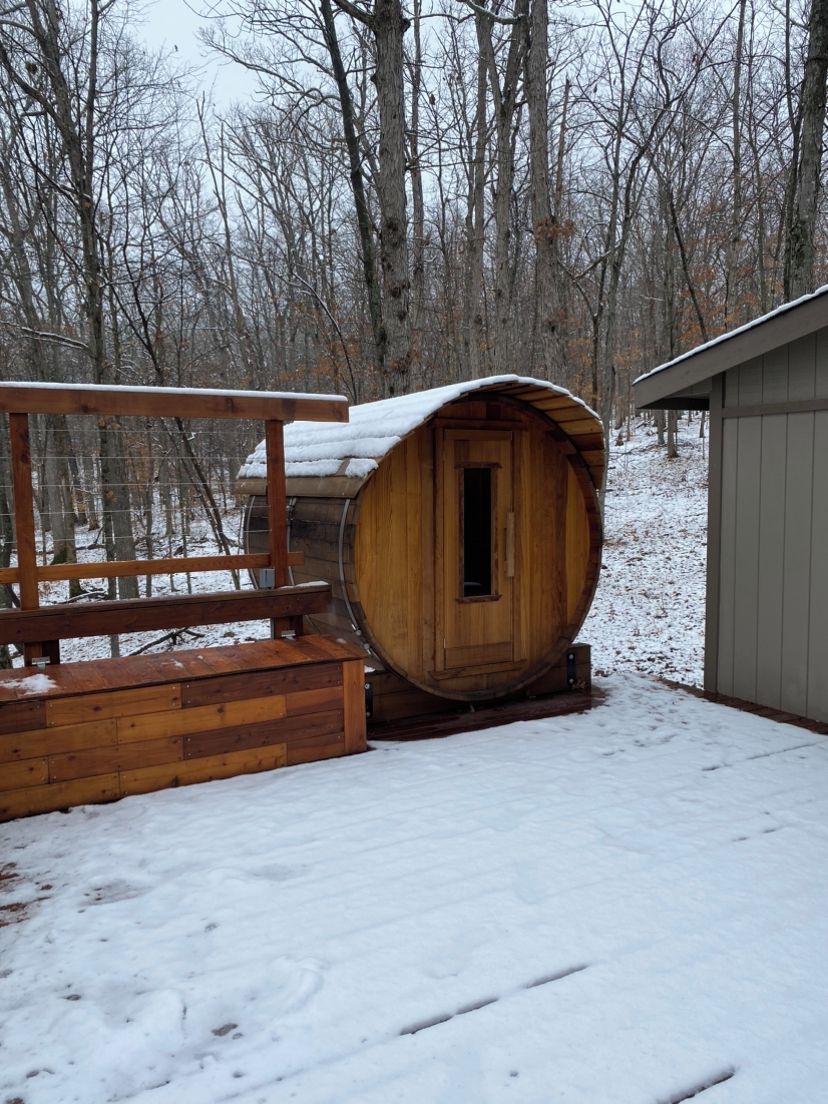 Una struttura a botte in legno con una porta, circondata da un pontile in legno e una recinzione metallica.