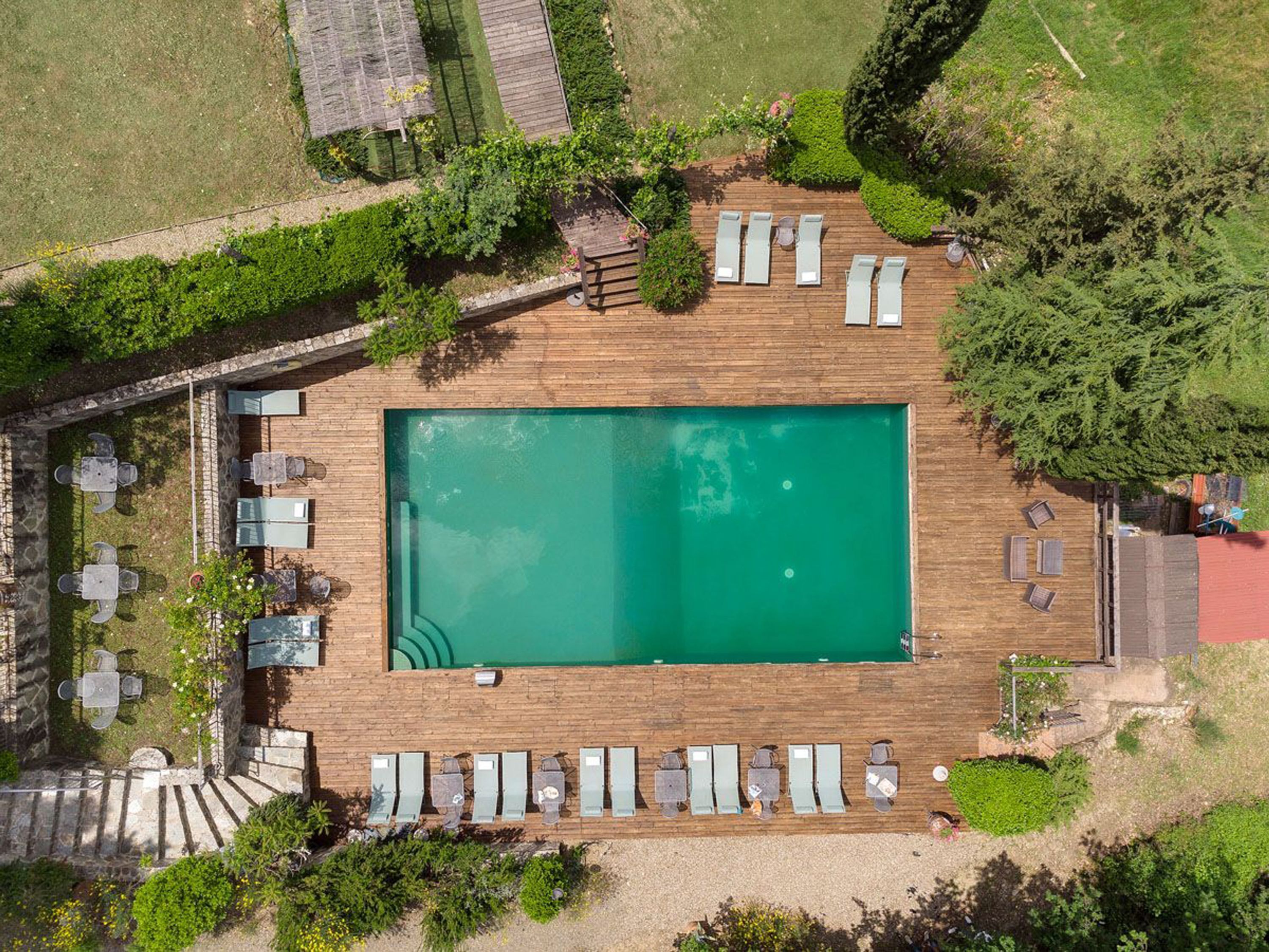 An aerial view of a rectangular swimming pool surrounded by a wooden deck with lounge chairs and tables.