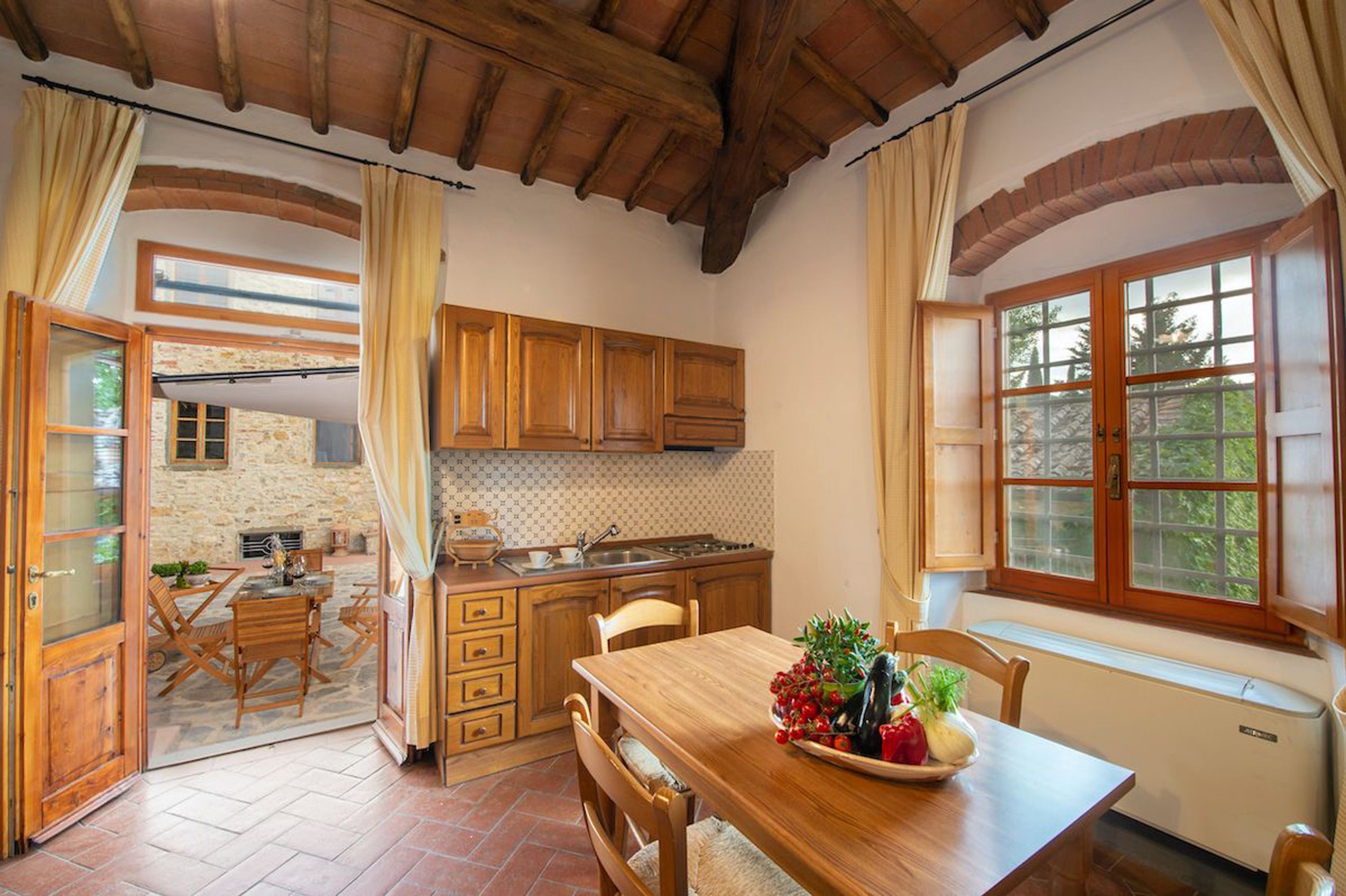 A rustic kitchen with wooden cabinets, a dining table with chairs, and a window with curtains.