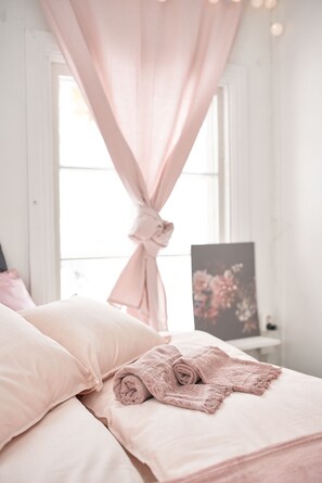Een slaapkamer met een bed, een raam met gordijnen en een schilderij aan de muur.