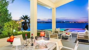 Une terrasse aménagée avec un coin repas, donnant sur une étendue d’eau au crépuscule.