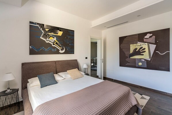 Ein modernes Hotelzimmer mit einem großen Bett, einem Nachttisch und zwei abstrakten Bildern an den Wänden.