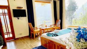 Ein Zimmer mit Bett, Fernseher, Esstisch, Stühlen und Blick ins Freie.