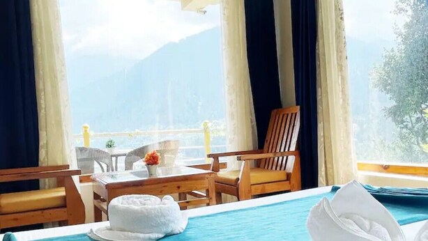 Ein Hotelzimmer mit Bett, einem Holztisch mit Stühlen, einem Fenster mit Vorhängen und Bergblick.