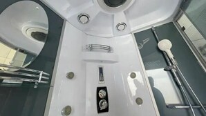 Ein modernes Badezimmer mit Duschkabine aus Glas, Handbrause und Bedienfeld mit Knöpfen.