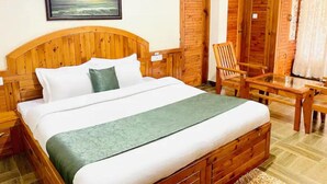 Een bed met houten frame, witte beddengoed, een groene plaid en een foto van een zonsondergang aan de muur.