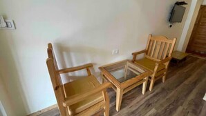 A room with a wooden floor, two wooden chairs, a small glass table, and a wall-mounted light fixture. - Spacious Wooden Room w/ Attic Olive Manali Cottage (Manali)