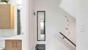 Un couloir moderne avec un meuble en bois, un petit banc noir et un miroir accroché au mur.
