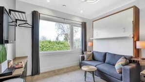 Un salon moderne avec un canapé gris, une petite table basse ronde, un téléviseur fixé au mur et une fenêtre avec des rideaux.