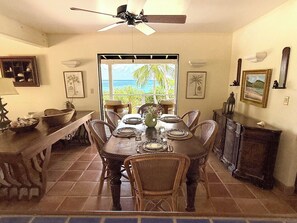 A dining area with a table set for four, a ceiling fan, and a view of the ocean through a large window.