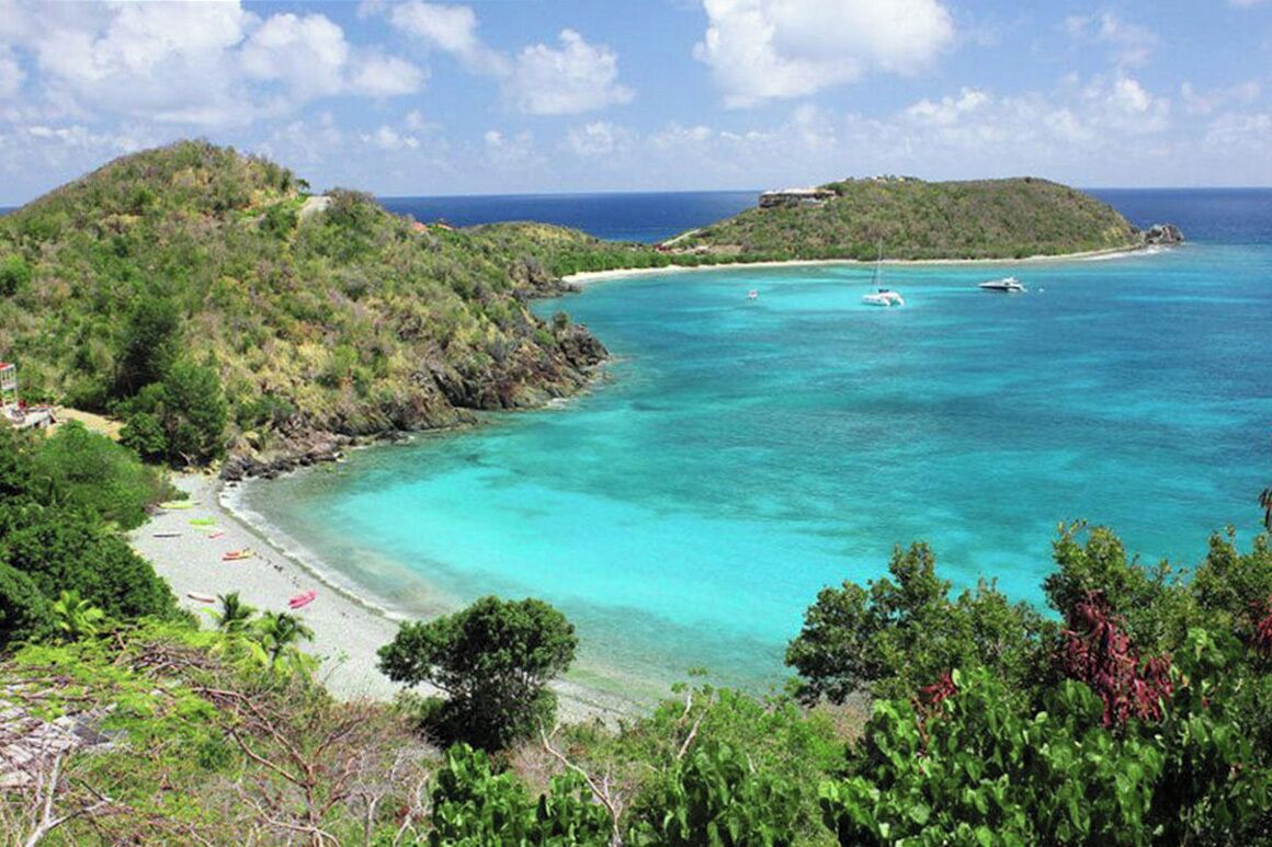 Un paysage côtier avec une plage, des eaux turquoise et limpides, et une végétation luxuriante.