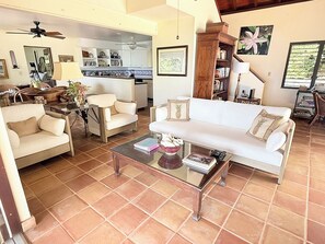 Ein Wohnzimmer mit Sofa, Sesseln, einem Couchtisch und einer Küche im Hintergrund.
