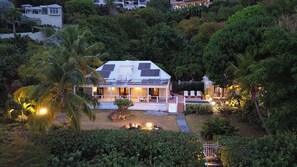 A house with a solar panel roof, surrounded by lush greenery and palm trees.