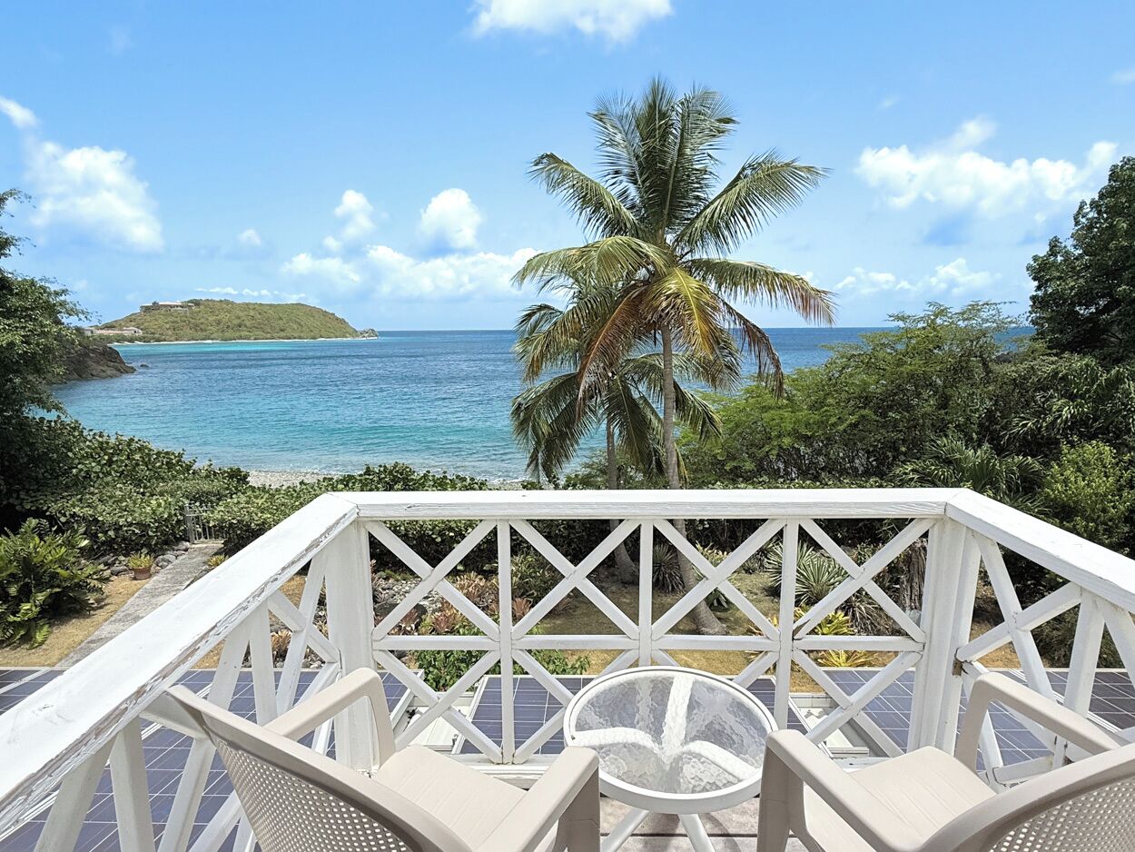 A deck with a view of a beach and ocean, surrounded by greenery.
