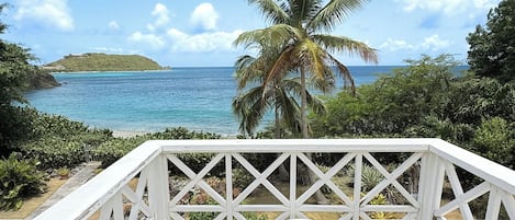 A deck with a view of a beach and ocean, surrounded by greenery.