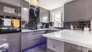 Una cocina moderna con una isla grande, salpicadero de baldosas negras, electrodomésticos de acero inoxidable e iluminación bajo los armarios.