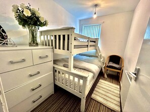 A bunk bed with a wooden frame, a dresser with drawers, a chair, and a vase with flowers. - Mordenised 2 Bedroom House Close to City Centre (Leeds)