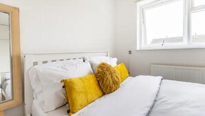 Un dormitorio con cama blanca, almohadas blancas y un cojín amarillo.