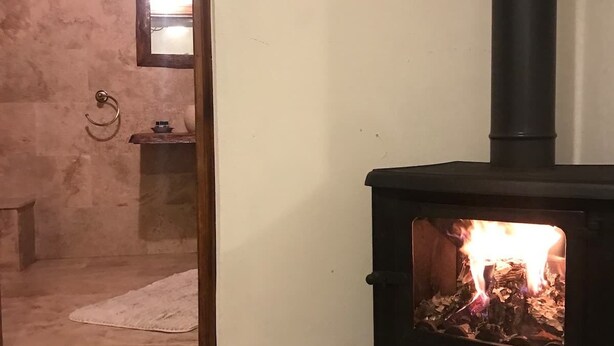 Een kamer met een houtkachel, een betegelde vloer en een klein raam.