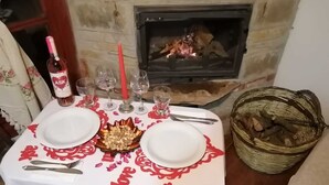 Een eettafel gedekt met borden, glazen en een fles wijn, met een open haard op de achtergrond.
