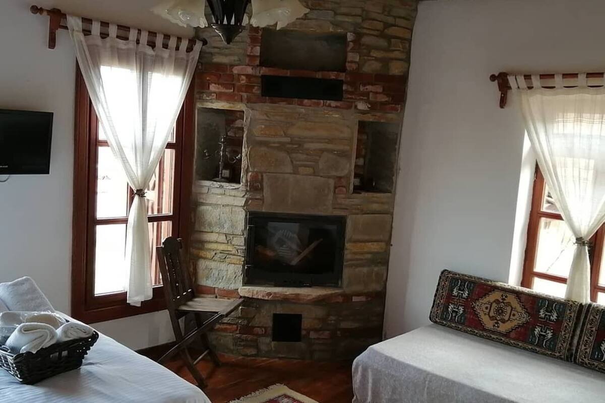 A cozy room with a stone fireplace, two white beds with patterned headboards, a wooden ceiling, and a red and white rug.