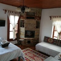 Una habitación acogedora con chimenea de piedra, dos camas blancas con cabeceros estampados, techo de madera y alfombra roja y blanca.