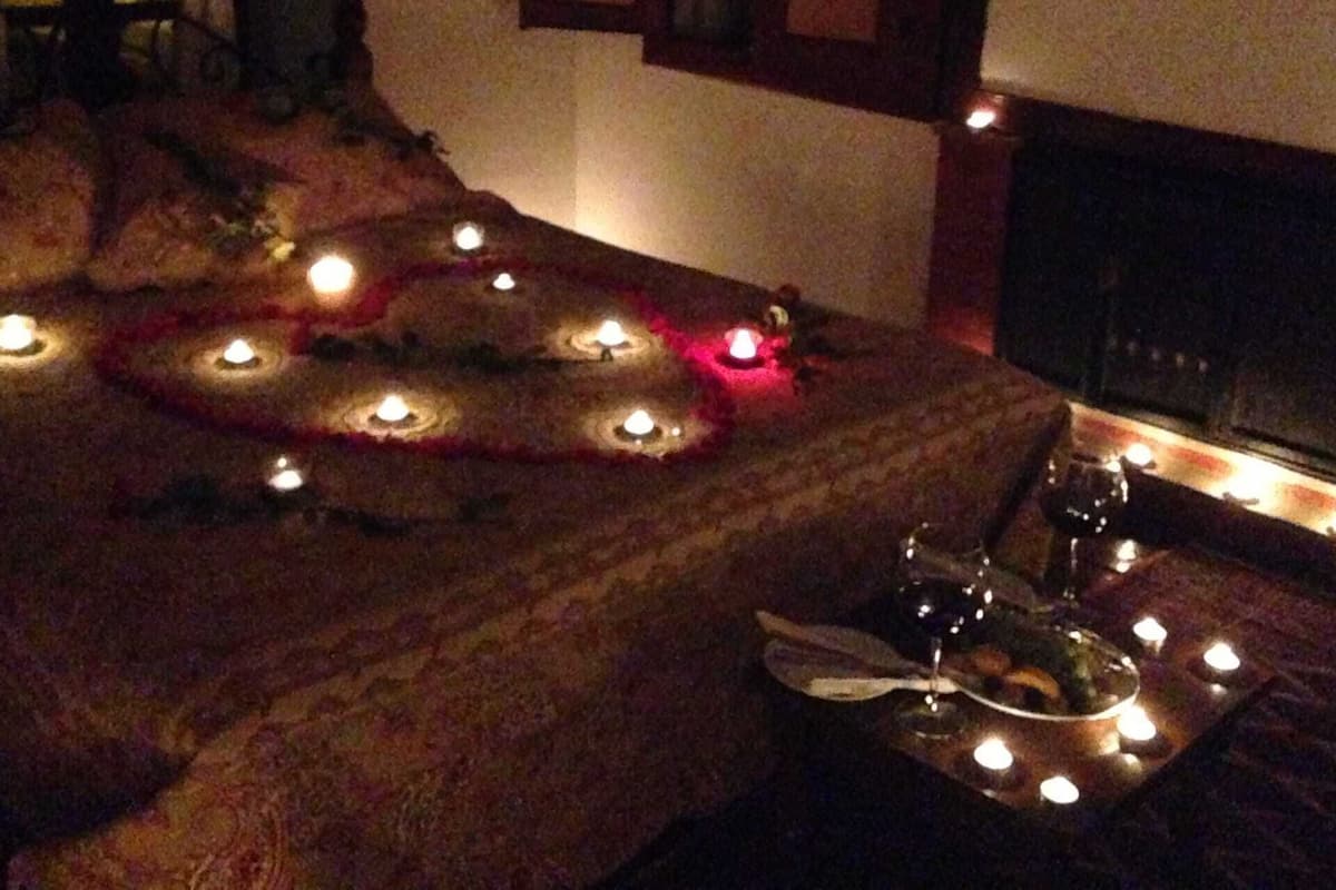 A dimly lit room with a bed, candles, and a tray of wine glasses.