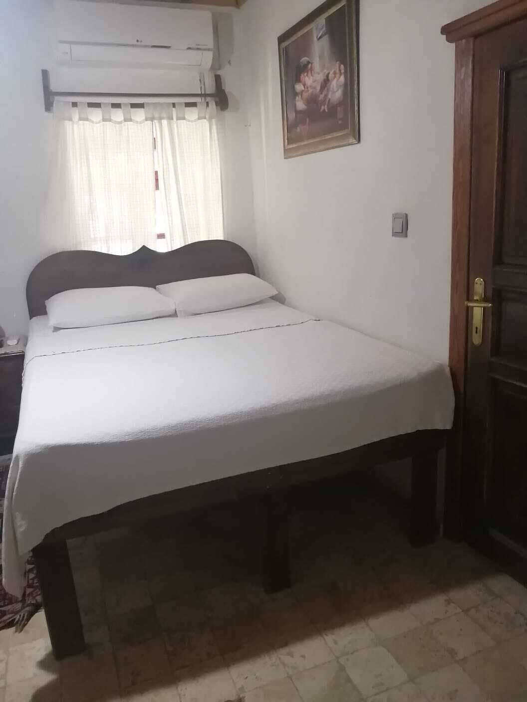 Un dormitorio con cama, aire acondicionado, una puerta y un cuadro colgado en la pared.