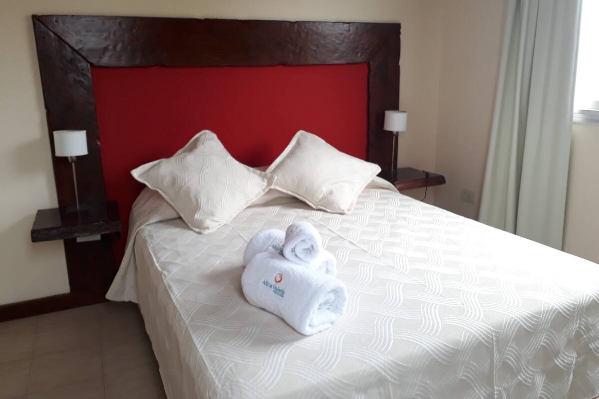 A hotel room with a red headboard, two white pillows, a neatly folded white towel, and two bedside lamps.