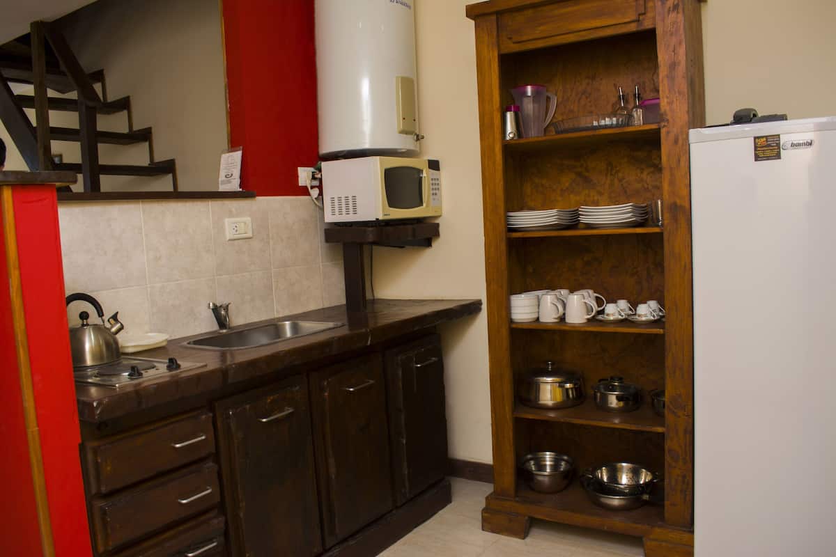 A kitchen with dark wooden cabinets, a white refrigerator, a microwave, and a wooden shelf with dishes and cookware.