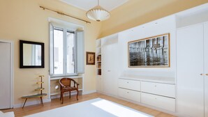 Ein Schlafzimmer mit einem großen Bett, einem Fenster mit Fensterläden, einem Sessel, einem Kleiderschrank und einem gerahmten Bild an der Wand.