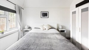 Une chambre à coucher avec un grand lit, deux tables de chevet, une commode, une armoire et une fenêtre avec des rideaux.