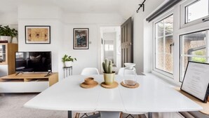 Un salon moderne avec une table à manger blanche, un téléviseur à écran plat et un cactus servant de décoration centrale.