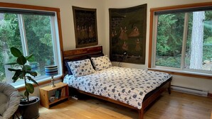 A bedroom with a wooden bed, large windows, a potted plant, and a rug. - Modern studio. (Salt Spring Island)