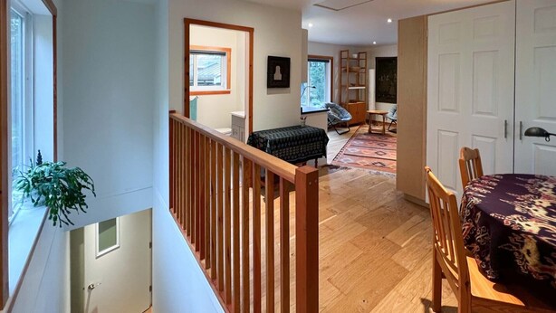A spacious living area with a wooden staircase, a dining table with chairs, a sofa, and a bookshelf. - Modern studio. (Salt Spring Island)