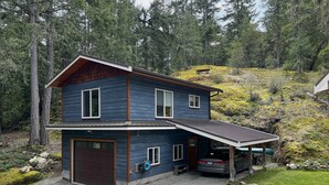 A two-story house with a garage, a covered porch, and a car parked in the driveway. - Modern studio. (Salt Spring Island)