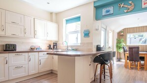 Una cocina con armarios blancos, encimera de madera, un taburete de bar y una mesa de comedor con sillas.