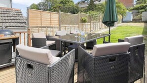 Un patio al aire libre con mobiliario de mimbre, una mesa y una parrilla.